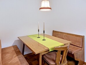 Ein Holztisch mit zwei Kerzen, einer grünen Tischläufer und einer Holzbänkl mit gepolstertem Sitz.