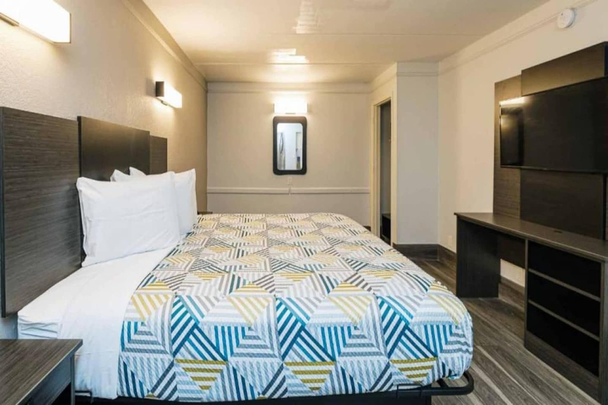 A hotel room with a bed, a TV, and a mirror.