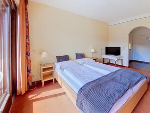 Une chambre d’hôtel avec un lit double, deux tables de chevet avec des lampes, un téléviseur posé sur un meuble et une grande fenêtre avec des rideaux.