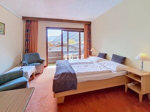 A hotel room with a bed, a desk, a chair, and a view of the mountains through a sliding door. - Vergissmeinnicht by Interhome (Sankt Ulrich am Pillersee)