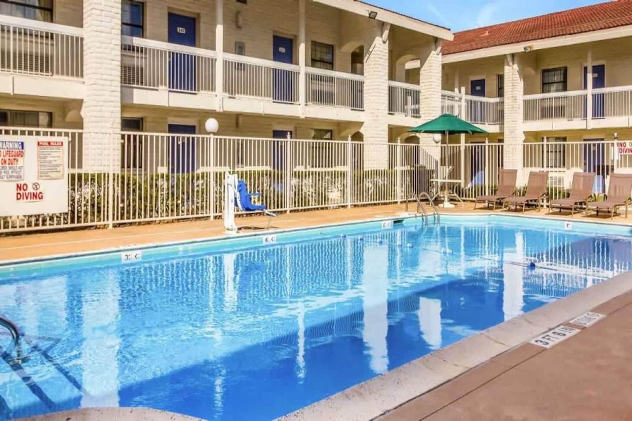 A swimming pool with a white fence, lounge chairs, and a building with multiple balconies.