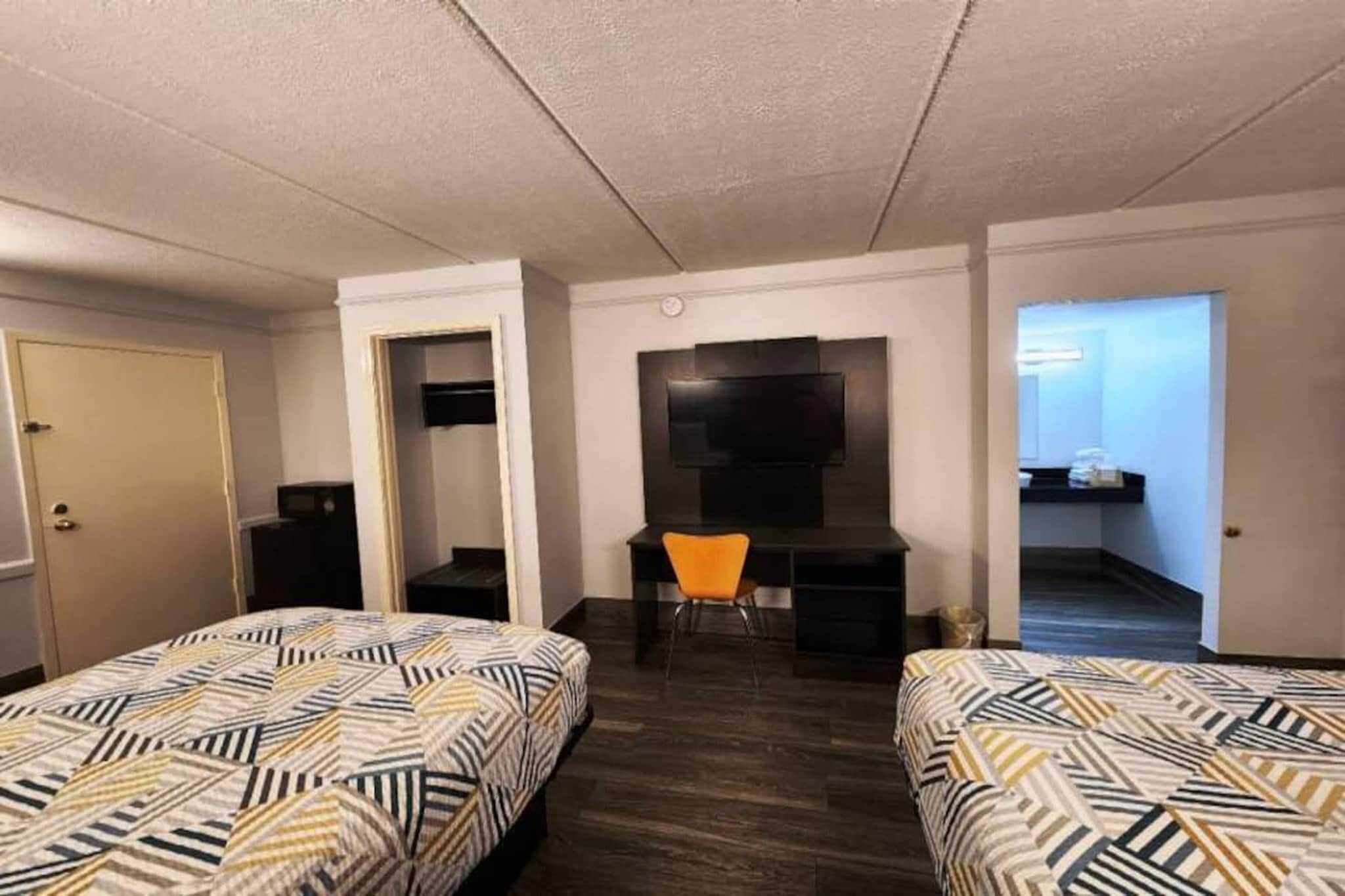 A hotel room with two beds, a desk, a chair, and a TV mounted on the wall.