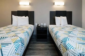 Una habitació d'hotel amb dos llits, cadascun amb un estovat estampat, una tauleta de nit entre ells i llums penjades a la paret.