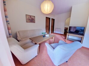 Ein Wohnzimmer mit einer Couch, einem Couchtisch, einem Fernseher und einem Bild an der Wand.