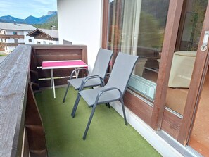 Een balkon buiten met een tafel en stoelen, een houten bank en uitzicht op bergen.