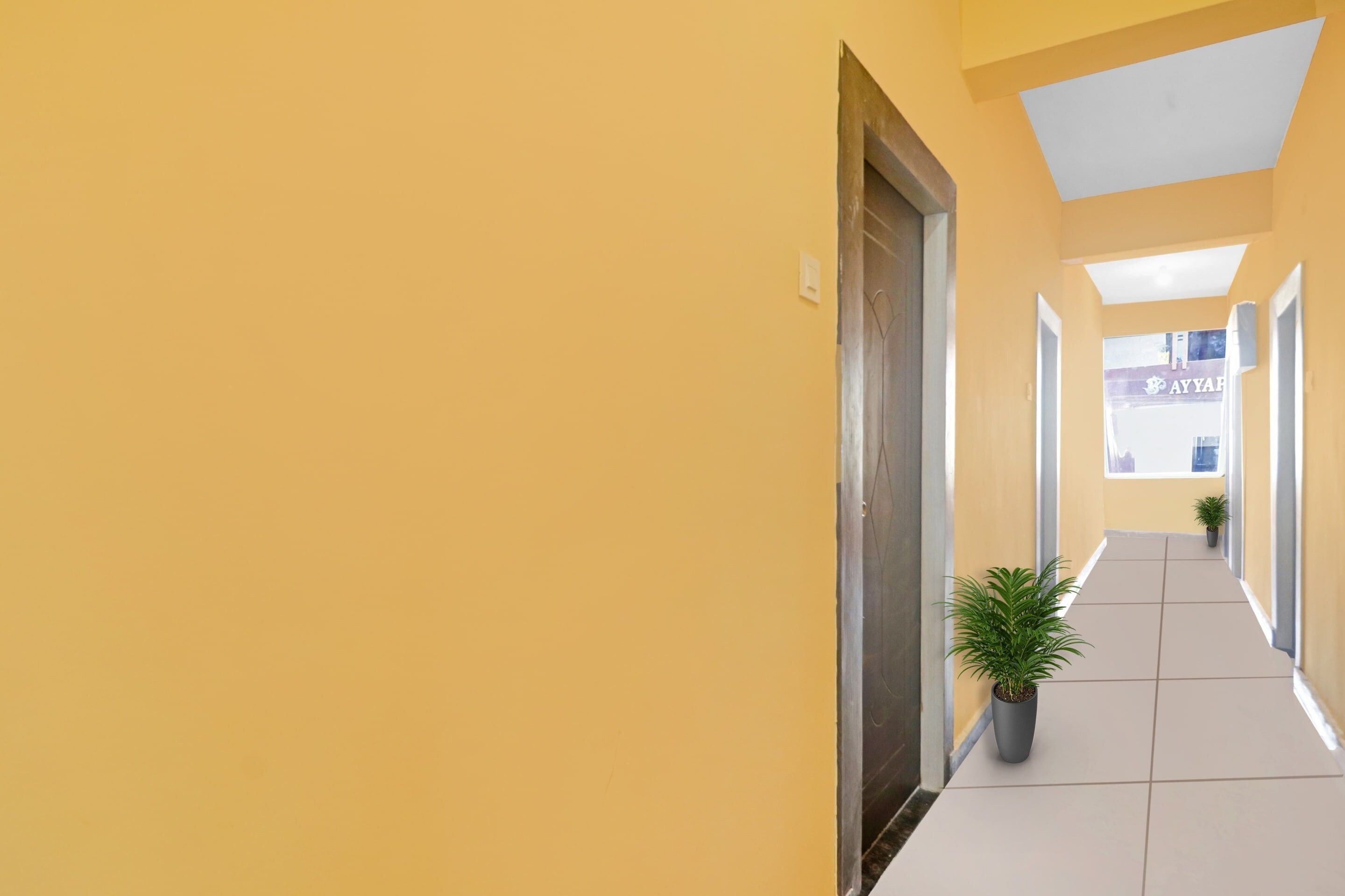 A corridor with yellow walls, a tiled floor, and potted plants.