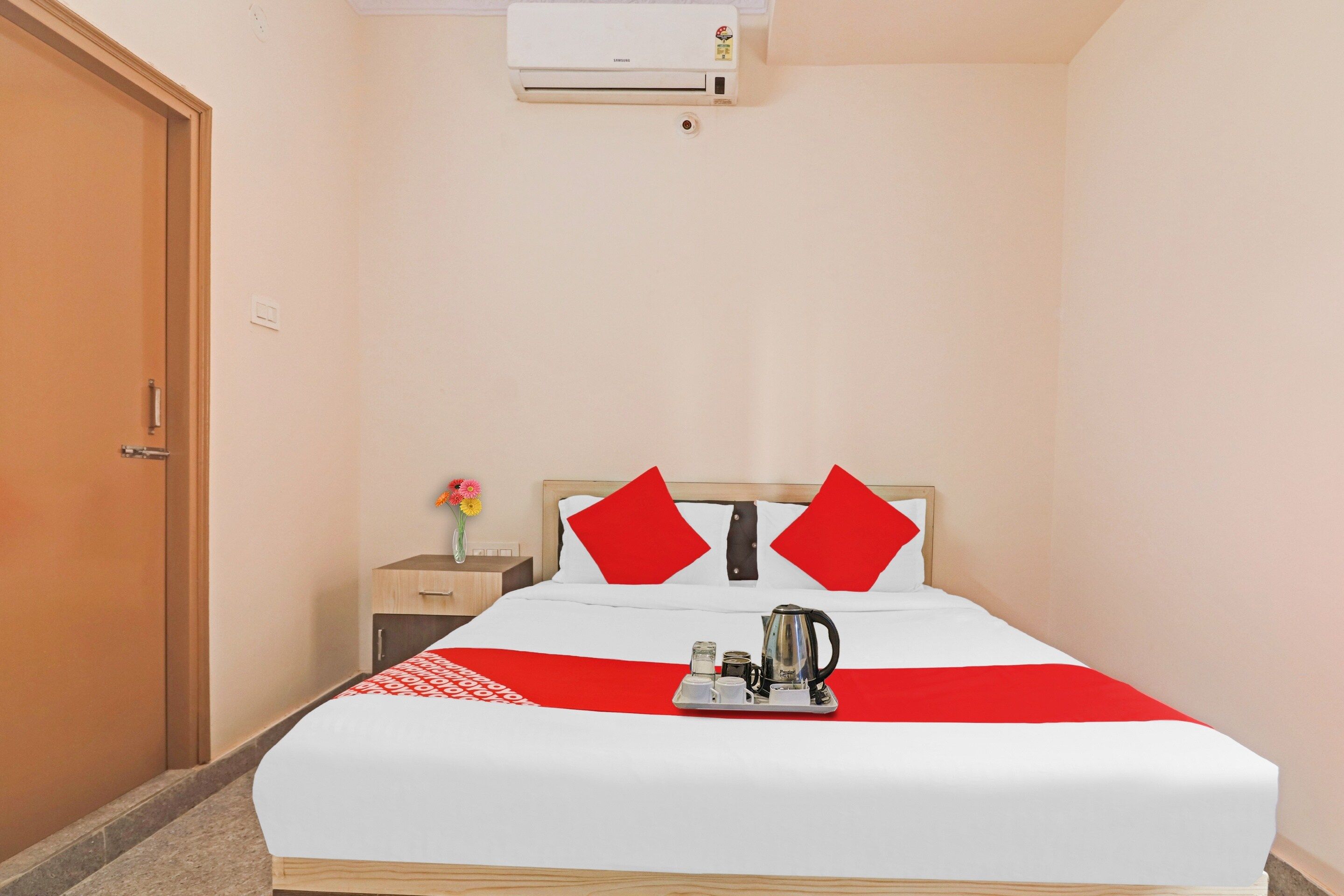A hotel room with a bed, a nightstand, a vase with flowers, and a coffee maker.