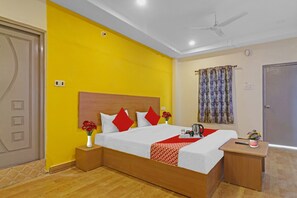 Quarto de hotel com cama, mesas de cabeceira, um ventilador de teto e janela com cortinas.