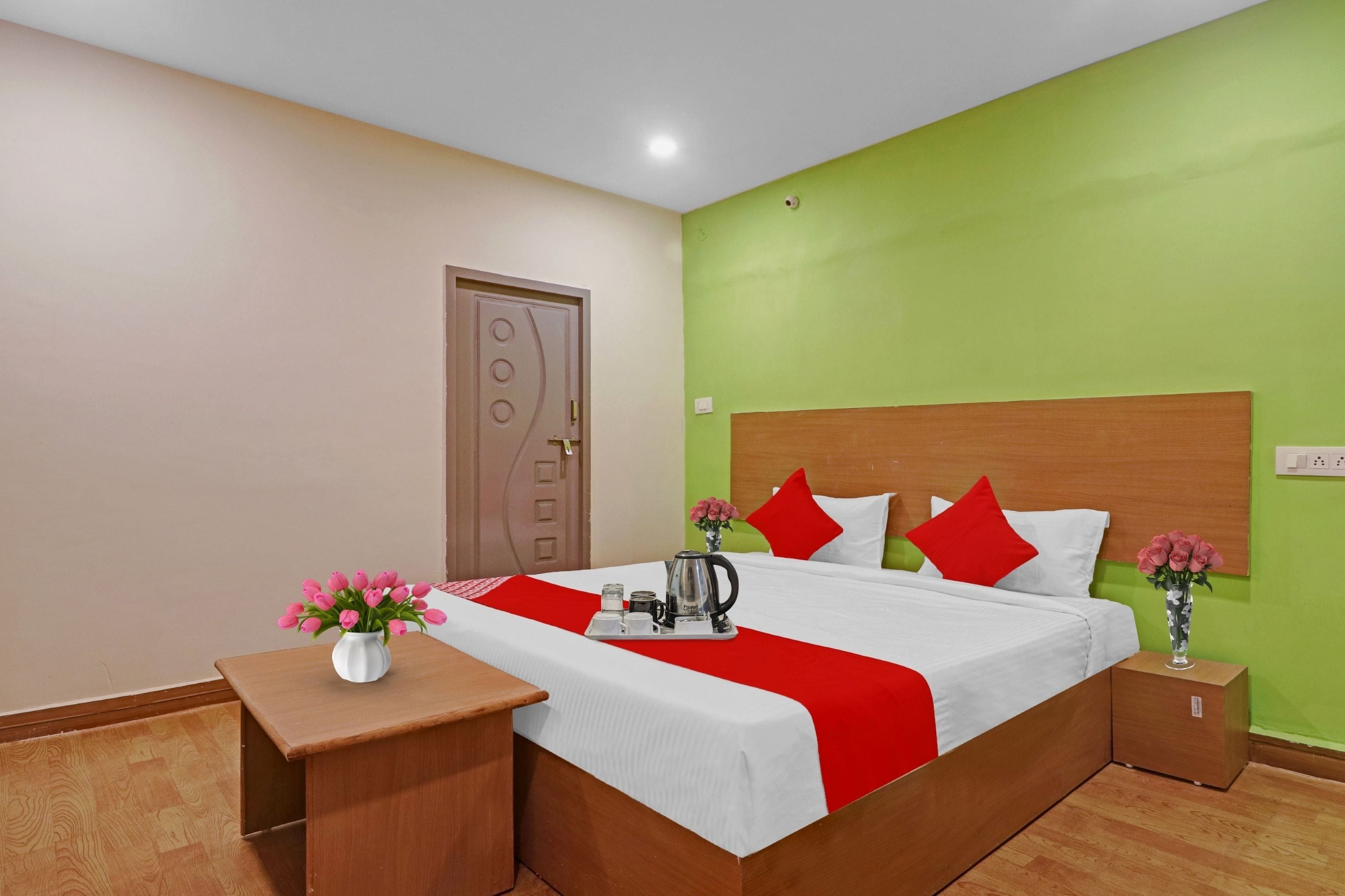 Una habitación de hotel con una cama, mesitas de noche, un florero con flores y una tetera.