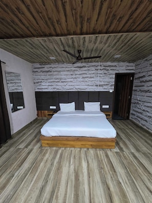 A bedroom with a wooden ceiling, a stone wall, a bed with white bedding, and a ceiling fan. - Hotel O Royal Palace (Amritsar)