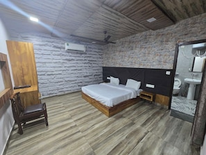 A bedroom with a bed, a wooden chair, a nightstand, a wall-mounted air conditioner, and a bathroom with a sink and toilet. - Hotel O Royal Palace (Amritsar)