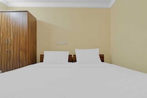 A hotel room with a bed, two pillows, a wooden wardrobe, and a wall socket. - Hotel O White Carnations Hotels (Hyderabad)