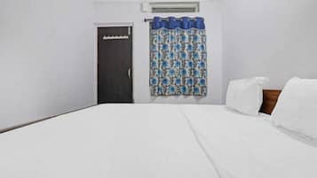Una cama individual con ropa de cama blanca, una puerta oscura y una ventana con cortina azul.