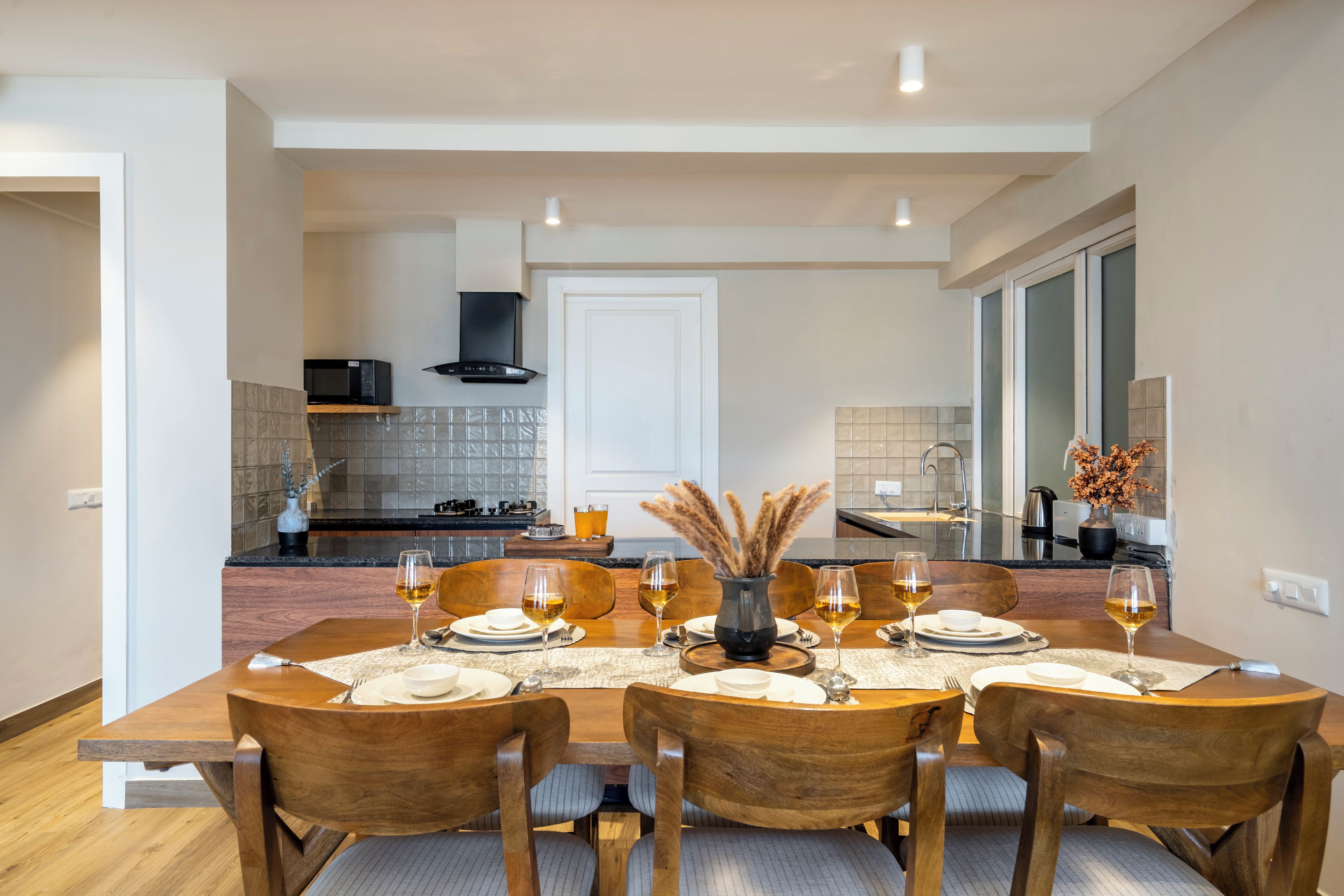 Un comedor con una mesa preparada para cuatro, una cocina al fondo y vista del salón.