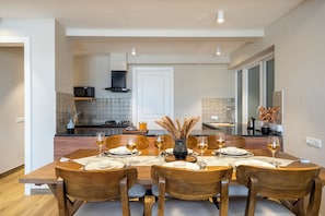 A dining area with a table set for four, a kitchen in the background, and a view of the living area. - Staymaster Solintra-Serviced Apartments (Nerul)