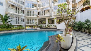 A multi-level residential building with a swimming pool, balconies, and potted plants.
