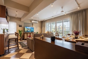 A modern kitchen with a dining area, large windows, and a flat-screen TV. - Staymaster Solintra-Serviced Apartments (Nerul)