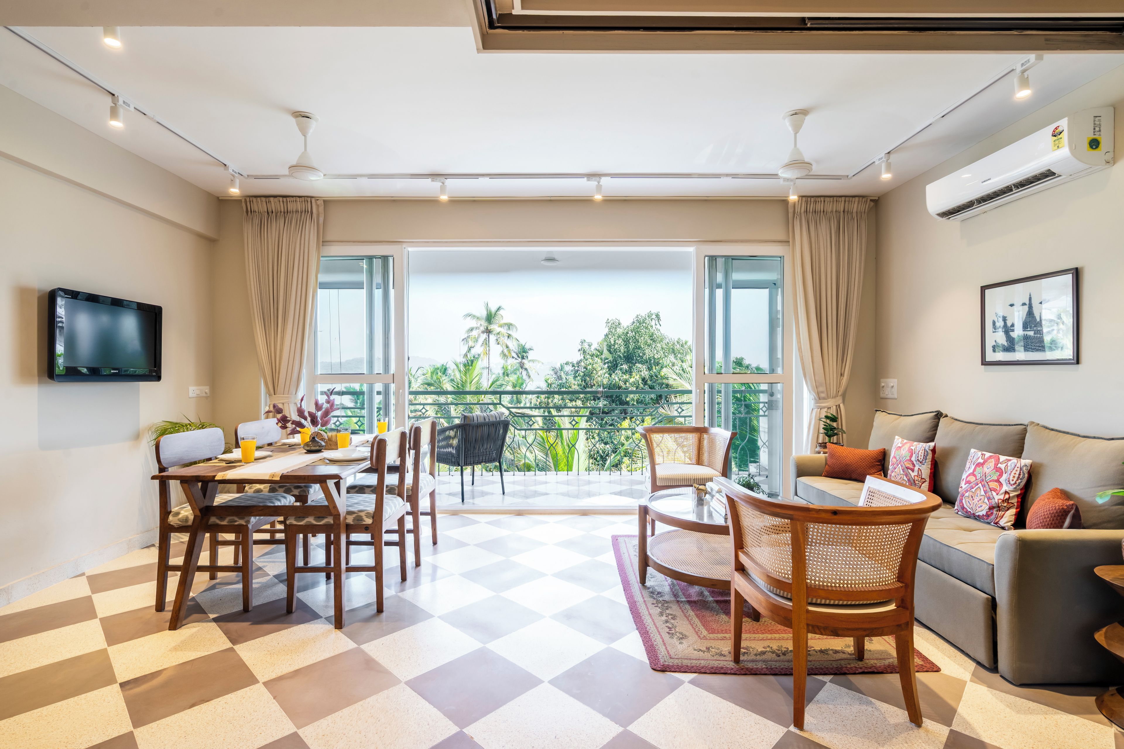 A spacious living area with a checkered floor, a balcony with a view, a sofa, and a dining table with chairs.