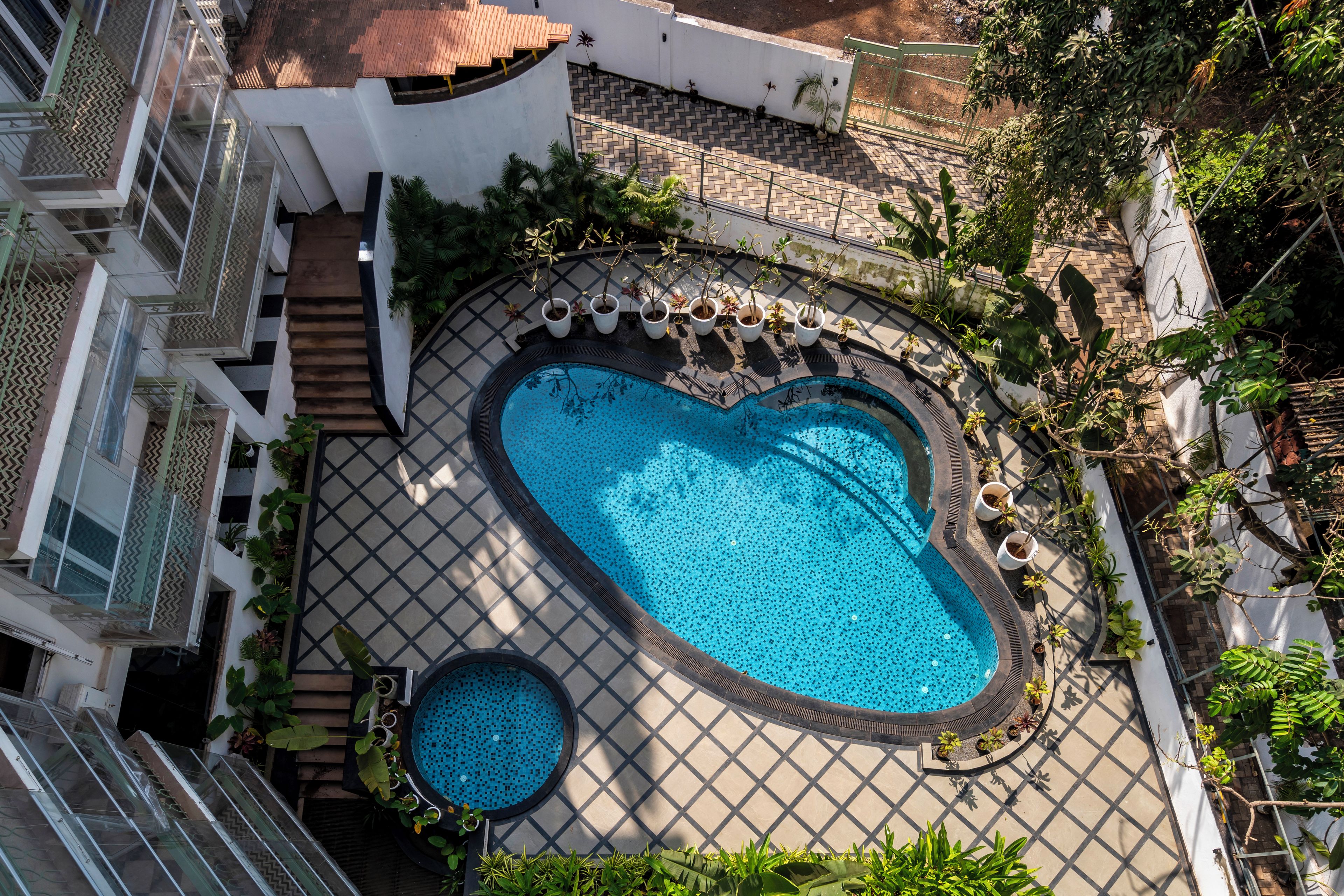A rooftop swimming pool with a heart-shaped design, surrounded by potted plants and a tiled deck.