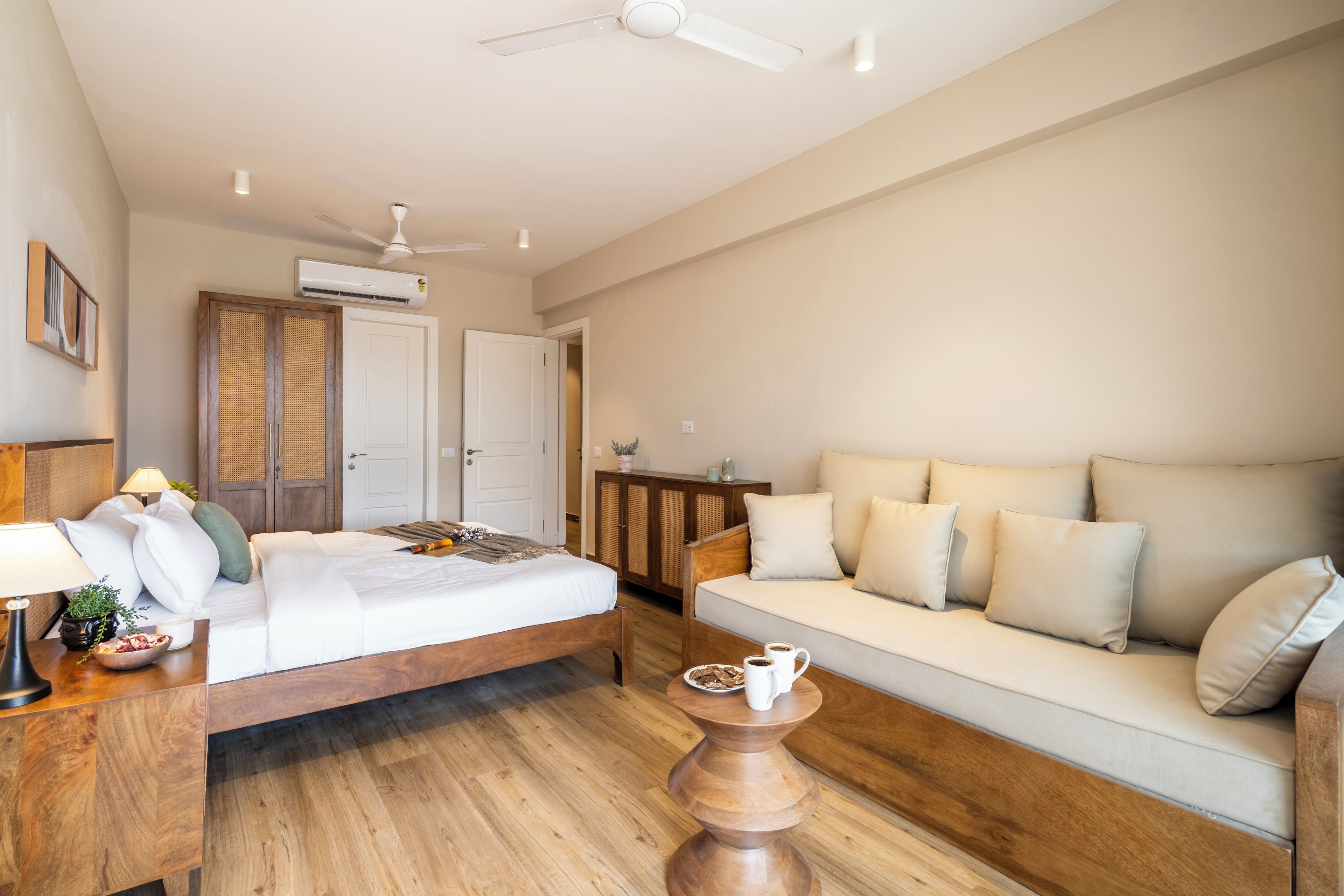 A hotel room with a bed, a sofa, a wooden coffee table, and a ceiling fan.