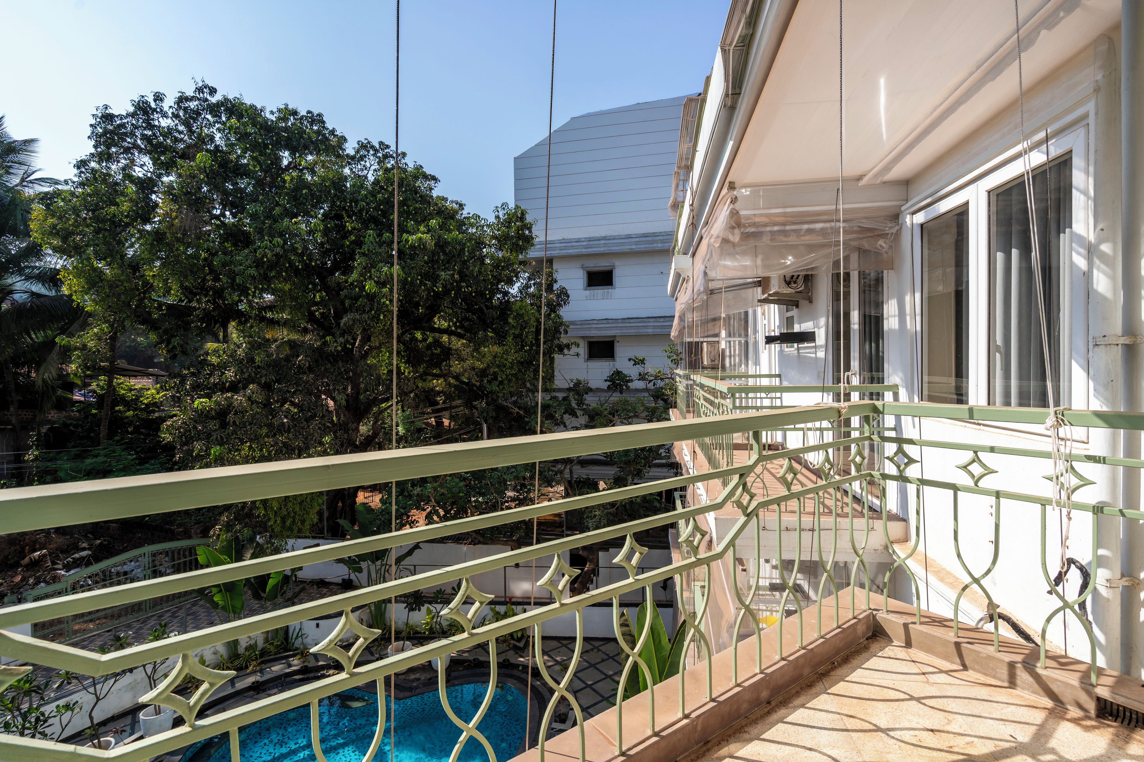 Ein Balkon mit Pool, umgeben von viel Grün und einem weißen Gebäude im Hintergrund.