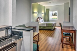 Ett hotellrum med en säng, ett skrivbord, en stol och ett litet kök.