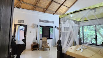 Una habitación con techo de paja, una cama con dosel, un ventilador y una silla.