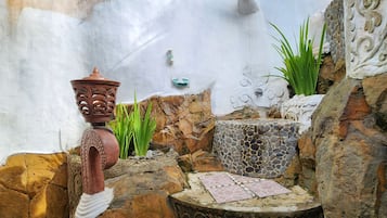 A stone-tiled patio with a decorative table, a rustic wall with a water spout, and a potted plant.
