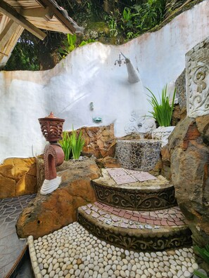Un patio empedrado con una mesa decorativa, una pared rústica con un caño y una planta en maceta.