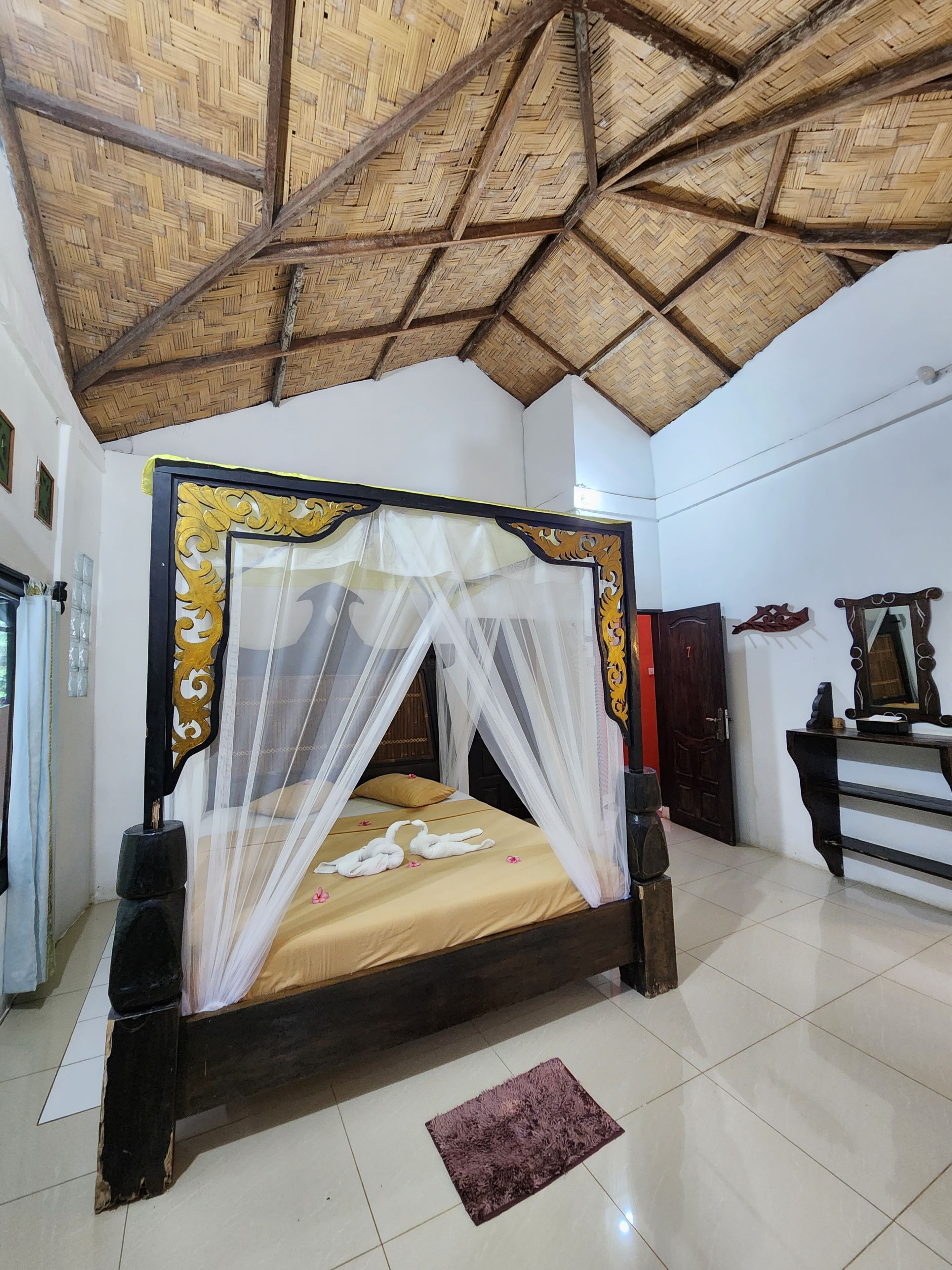 A room with a bed, a mosquito net, a wooden ceiling, and a tiled floor.