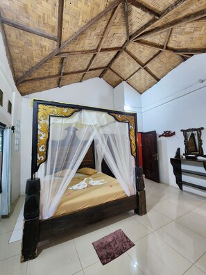 A room with a bed, a mosquito net, a wooden ceiling, and a tiled floor.
