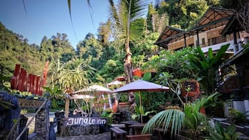 A Jungle Inn with outdoor seating, surrounded by lush vegetation and a mountain backdrop.