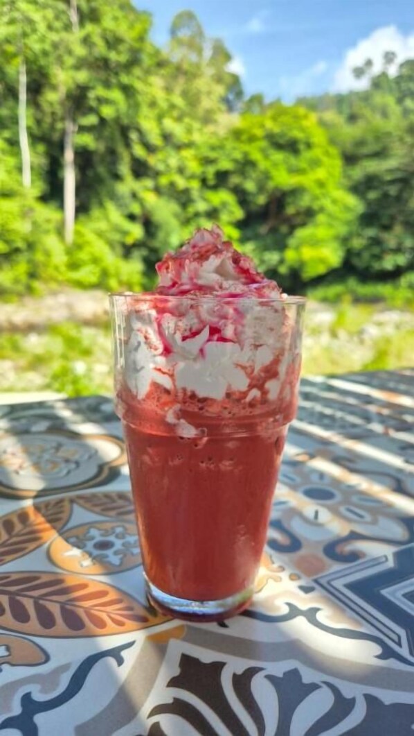 A glass with a red beverage and a white topping, placed on a patterned tablecloth.