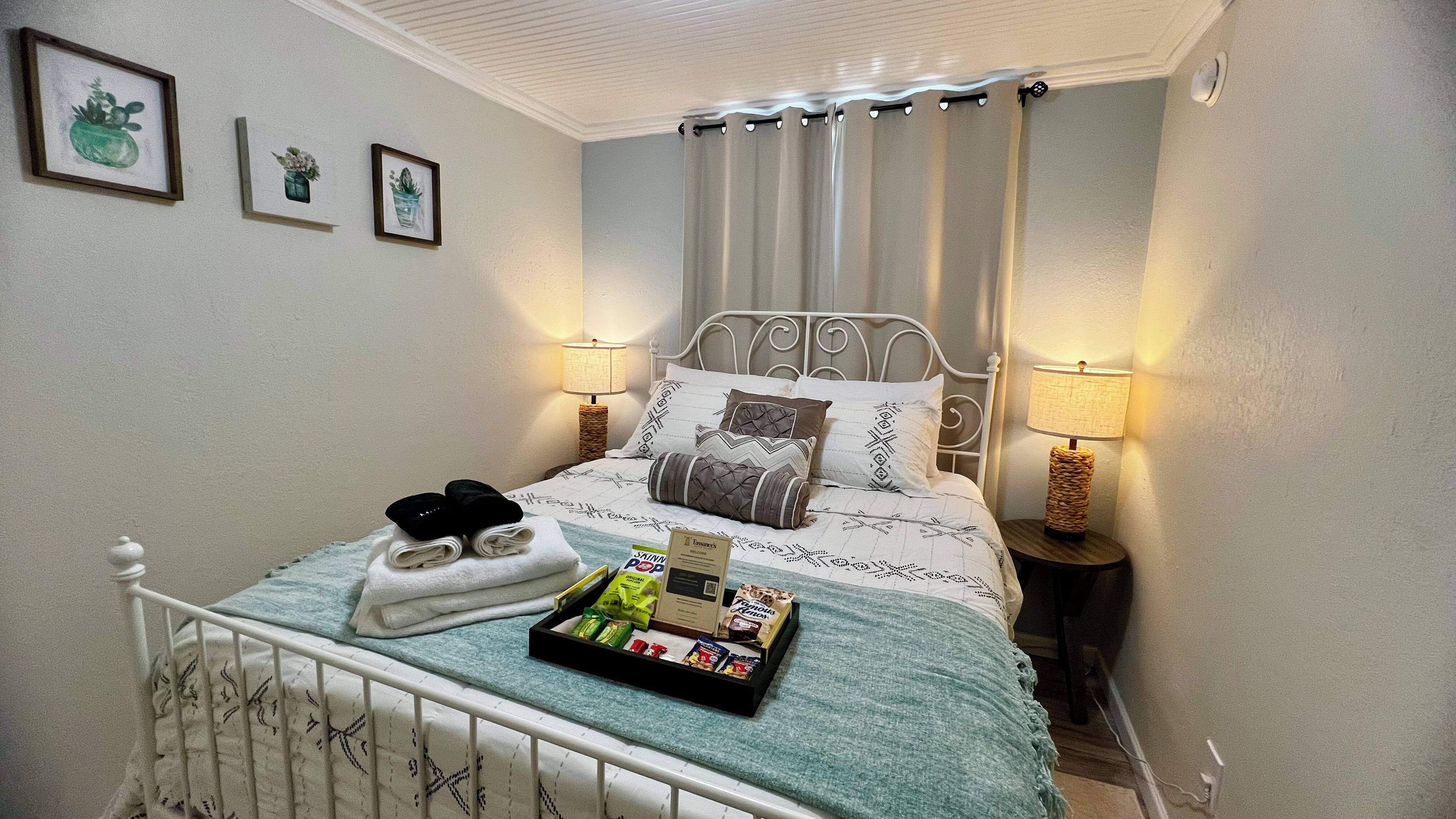 Een net opgemaakt bed met kussens, een dienblad met snacks en een set handdoeken.