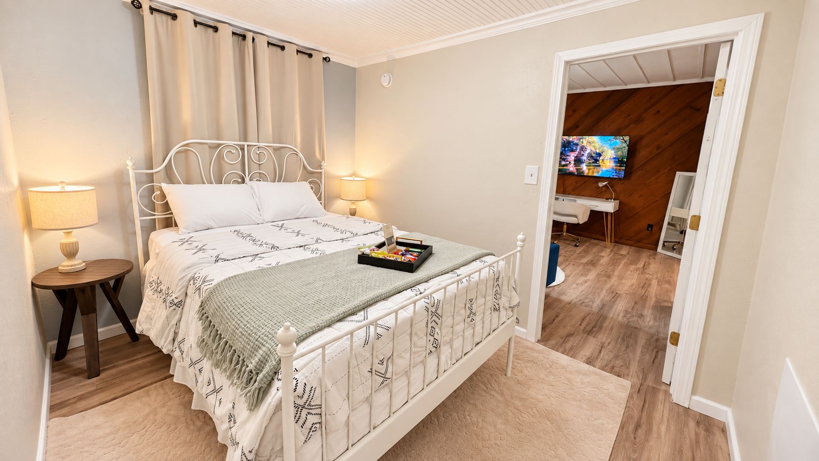 A bedroom with a bed, bedside lamps, a small table, and a painting on the wall.