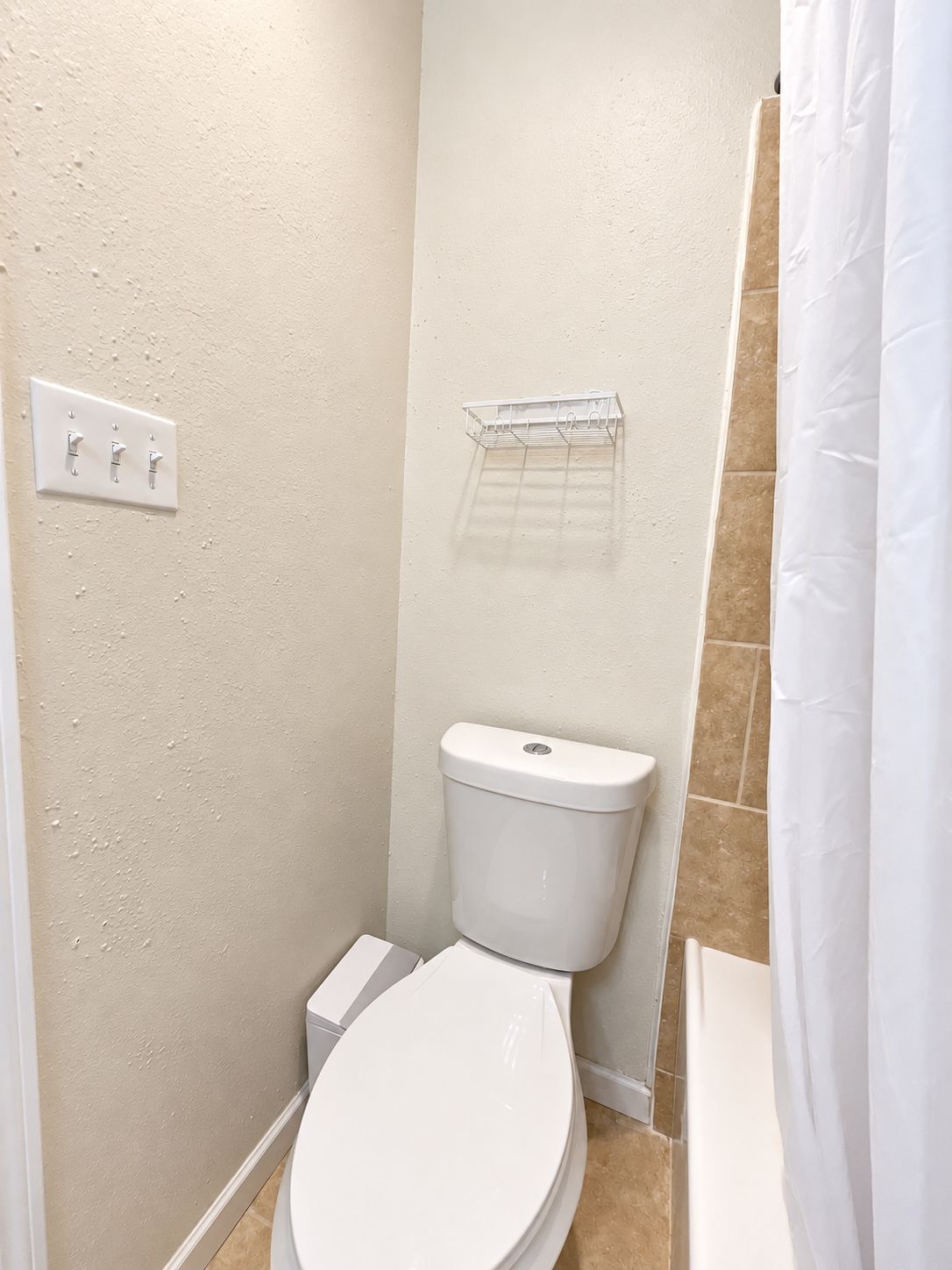 A small, compact bathroom with a toilet, a wall-mounted shelf, and a shower curtain.