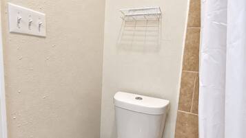 A small, compact bathroom with a toilet, a wall-mounted shelf, and a shower curtain.