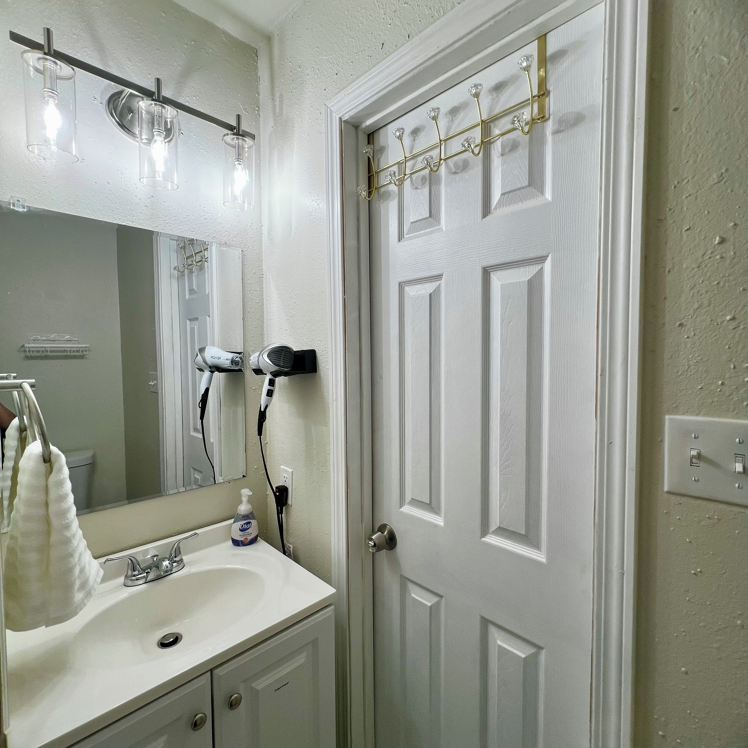 Un bagno con lavandino bianco, uno specchio, un asciugacapelli e un porta asciugamani.