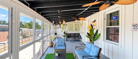 Une terrasse extérieure couverte, aménagée avec des meubles en osier, des ventilateurs de plafond et des plantes suspendues.