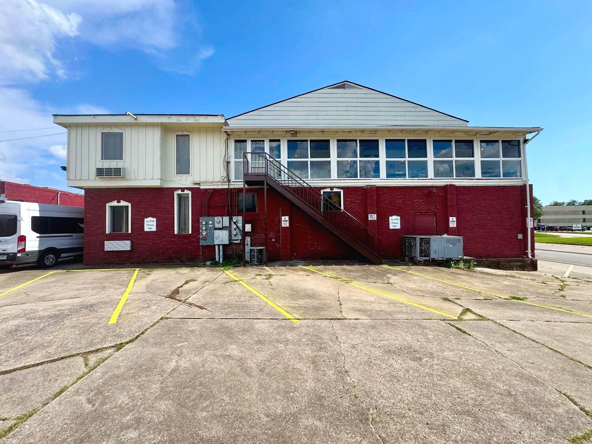 A red building with a white upper section, a staircase, and a parking lot with marked spaces.