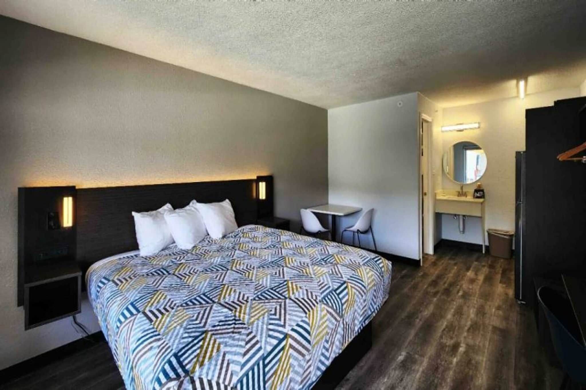 A hotel room with a bed, bedside tables, a desk, a chair, a mirror, and a wardrobe.