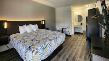 A hotel room with a bed, a desk, a chair, a TV, and a mirror.