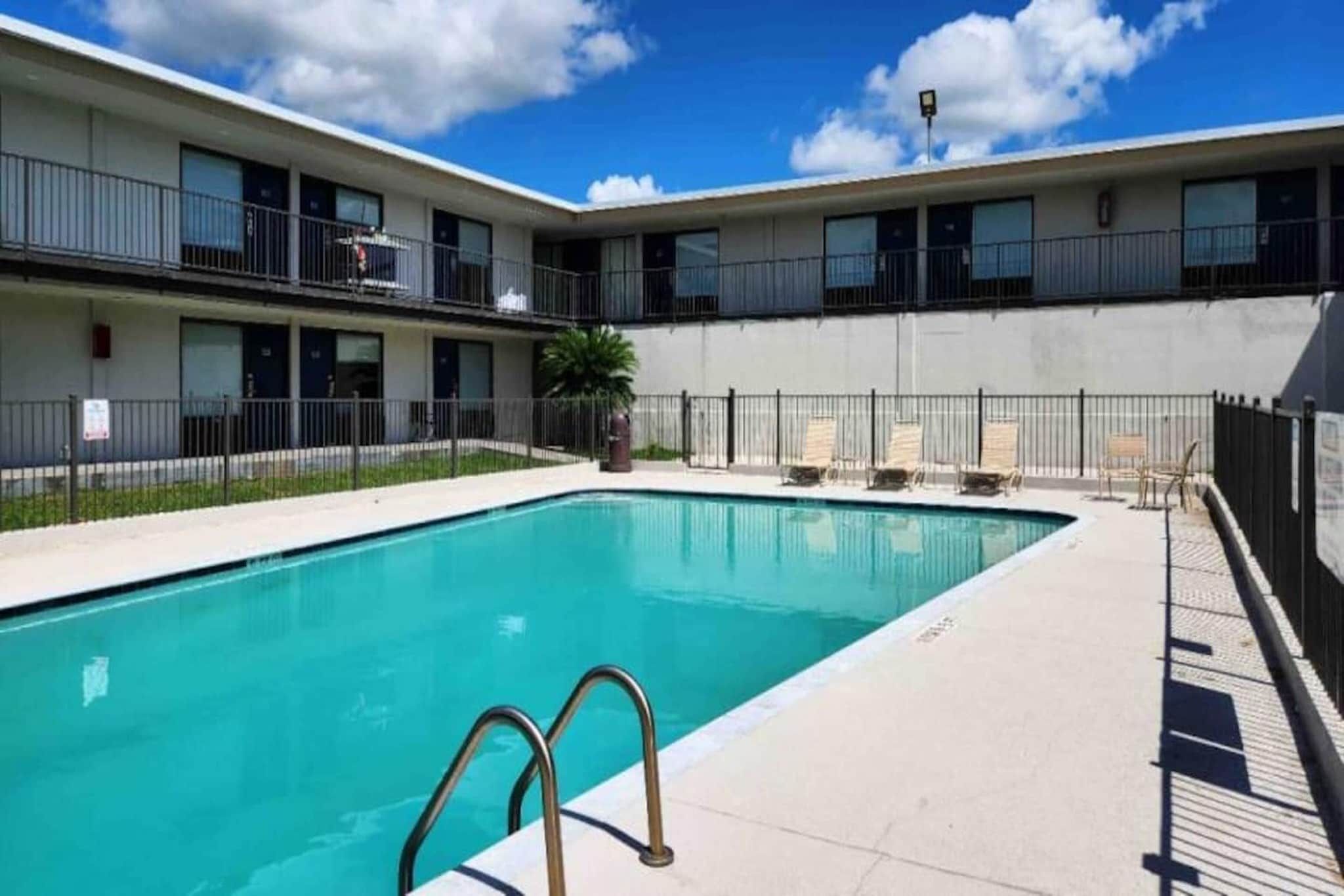 A rectangular swimming pool with a metal ladder in the foreground, surrounded by a fence.