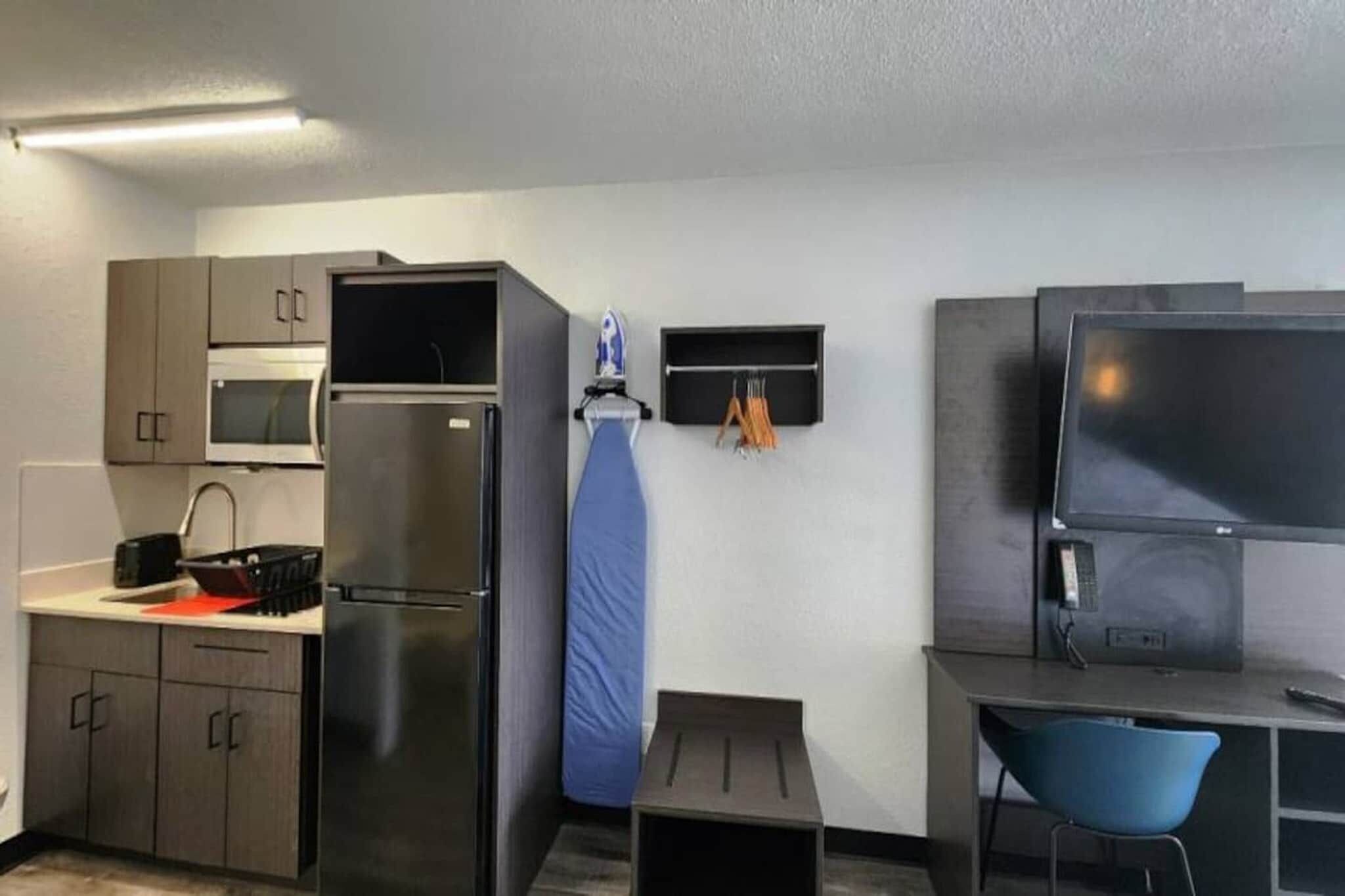 A compact kitchenette with a microwave, refrigerator, and a small ironing board.