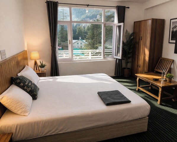 Habitación de hotel con una cama grande, un armario de madera, una mesita pequeña y una ventana que da a una casa y árboles.