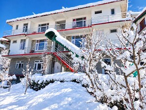 A multi-story building with a red and white exterior, a visible staircase, and snow-covered surroundings. - Apple Garden Aleo (Manali)