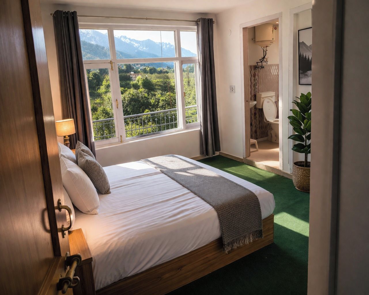 A hotel room with a large bed, a view of mountains, a bathroom with a toilet and sink, and a green carpet.