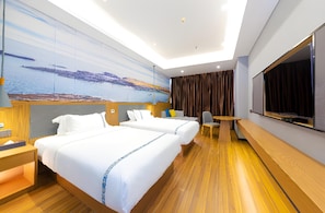Habitación de hotel con dos camas, un escritorio, una silla, un televisor y un ventanal con vistas al paisaje.