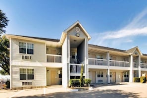 A multi-story motel with a central entrance, balconies, and a parking area. - Cozy 1 King Bed | Smoking (Dallas)