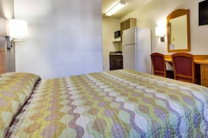 A hotel room with a bed, a desk, a chair, a refrigerator, and a microwave. - Cozy 1 King Bed | Smoking (Dallas)